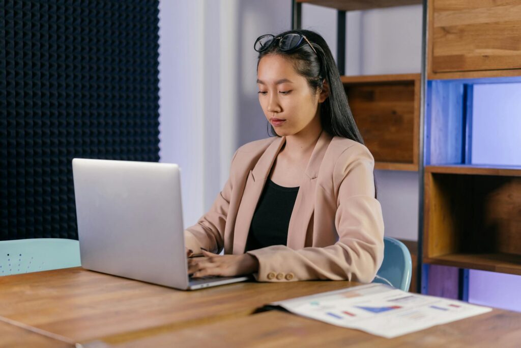 CMOs’ Creative Leap: Designing Meaning in an AI-Saturated Marketing World Asian businesswoman in a blazer typing on a laptop in a modern office setting - cmos creative leap