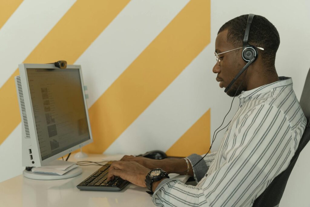 Domino’s Dom: How Conversational AI Drives Direct Revenue Growth Side view of a black man wearing glasses and headset working at a computer in an office - conversational ai revenue